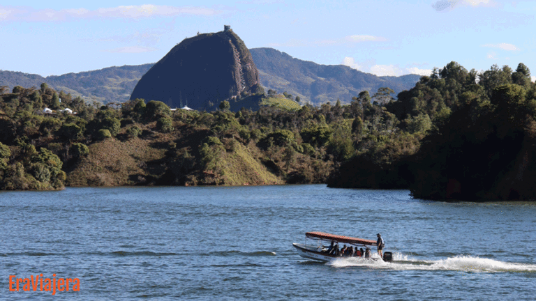 Barco navegando en el embalse de Guatapé con fondo de la piedra del peñol